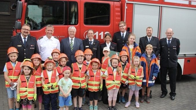 Blaulichtkids sind die Zukunft. Kindergruppe mit Bürgermeister und Feuerwehrfunktionären vor Feuerwehrauto.